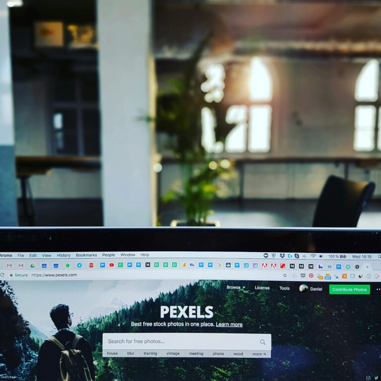 A close-up of a laptop displaying the Pexels website in a sunlit, modern office.